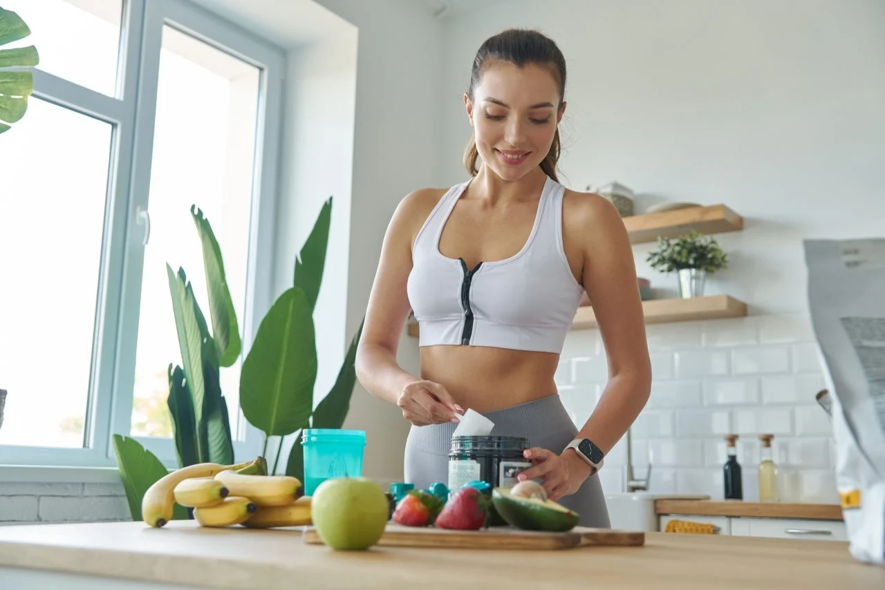 Happy Young Woman In Sports Clothing Preparing Protein Cocktail At Home.jpg